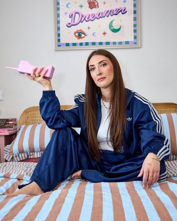 Woman sitting on bed holding pink book, relaxed and confident.
